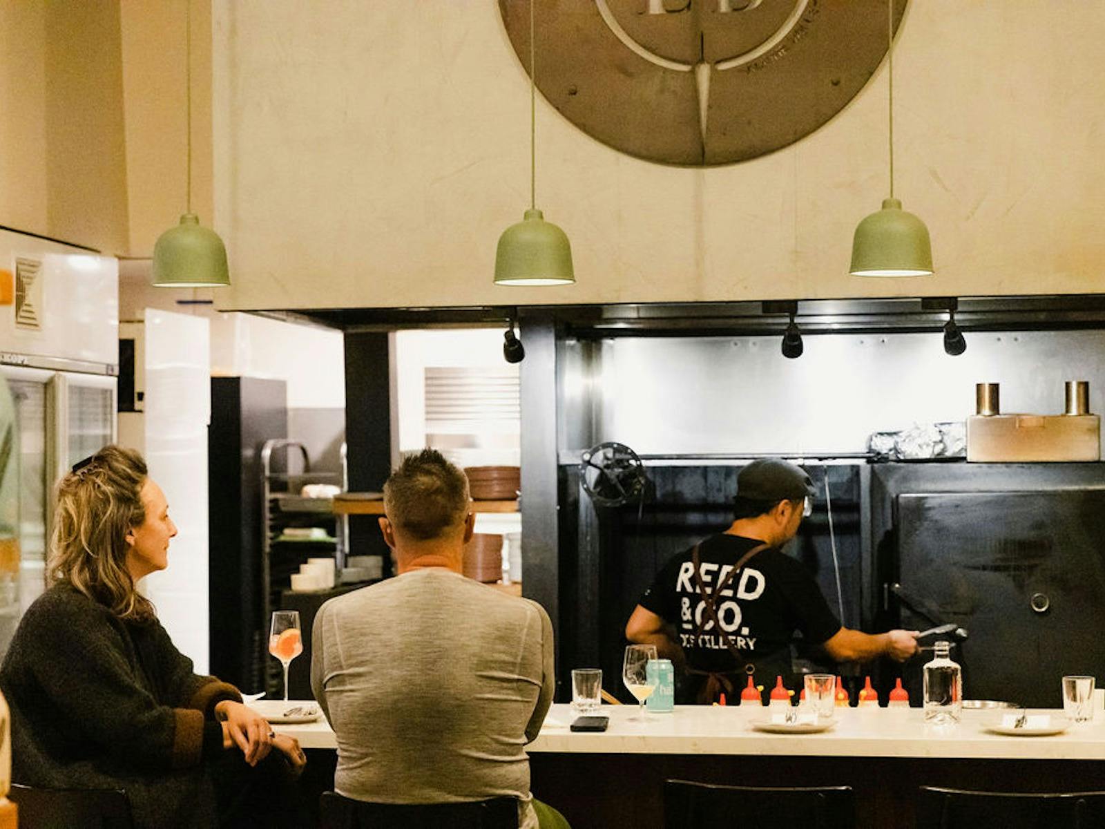 Two customers sit at a bar, watching a chef prepare their meals