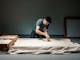 A man in a grey tshirt bends over a table of rice grains.