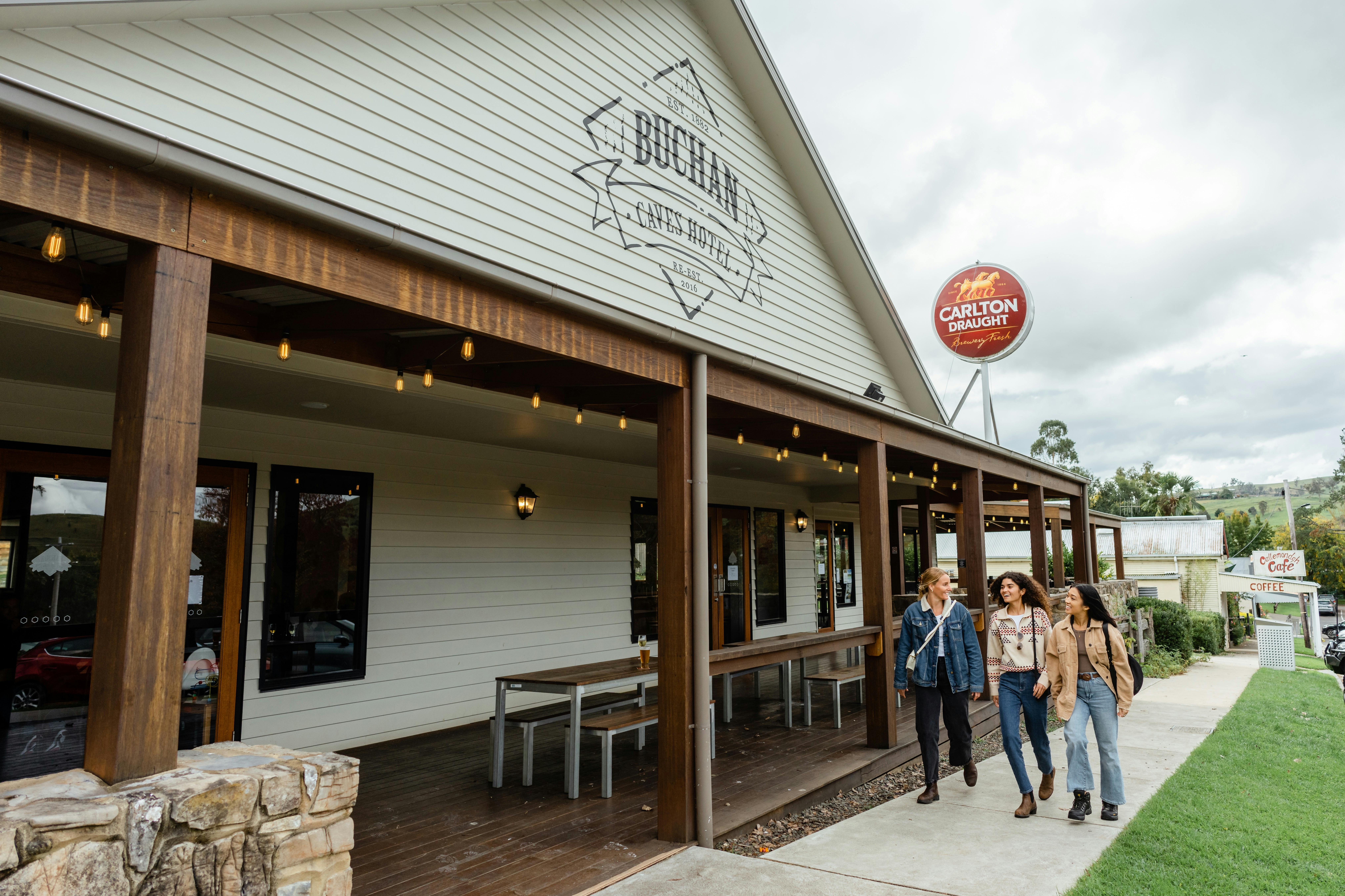 Three young women arrive at Buchan Pub, the Buchan Caves Hotel logo is featured above the awning