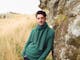 Man Leaning against rock in a grass field wearing Merinomink sweater
