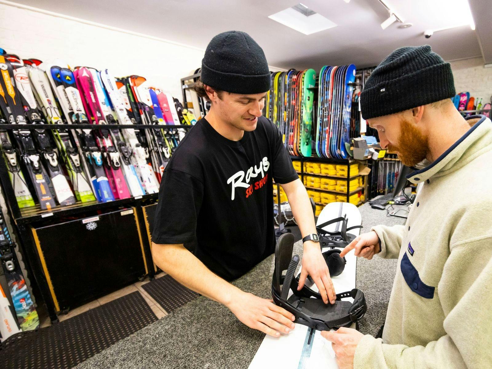 Staff member setting up snowboard at Ray's Ski Hire with guest