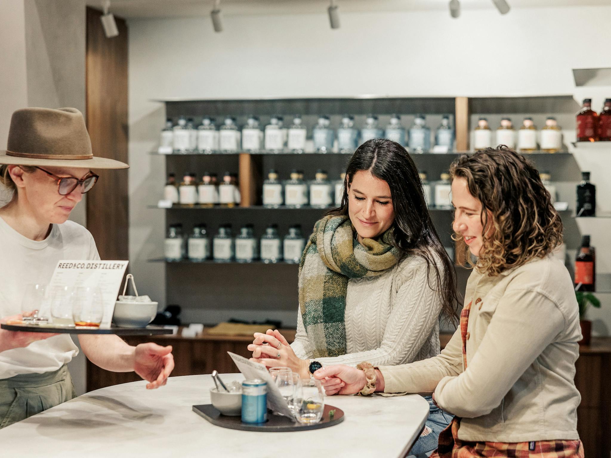 Two guests sit at a bar tasting drinks served by a staff member