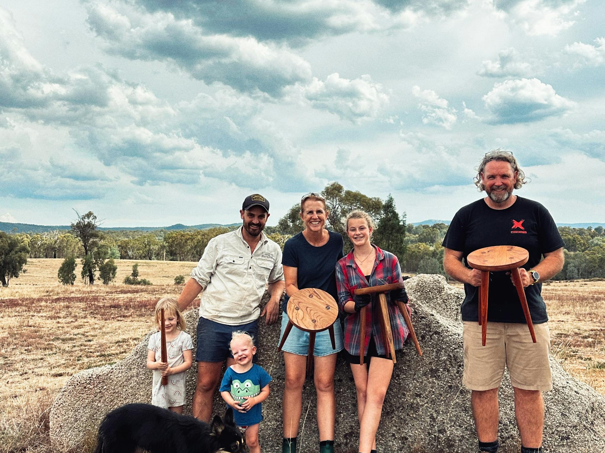 Three participants hold their stools in front of a rock