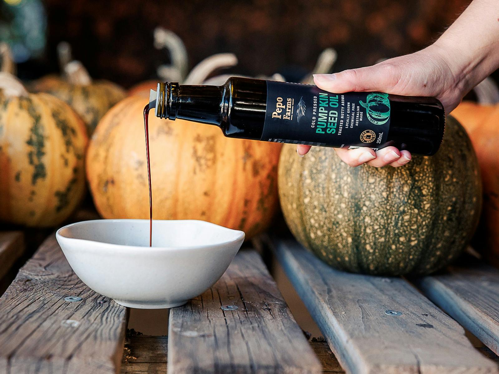 Pumpkin seed oil being poured into a bowl in front of harvested heirloom pumkins