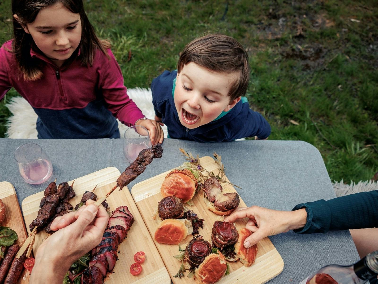 Wooden boards with assorted meats and two children eating