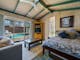 A pool house with a bed, couch and table. Swimming pool in the background outside.
