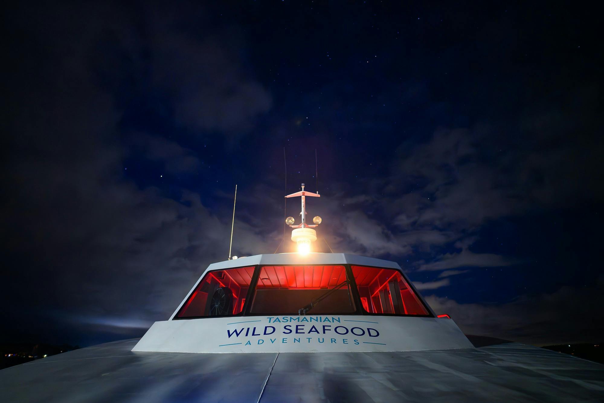 The wheelhouse of the vessel is illuminated with the red lights of the dashboard and darkness behind