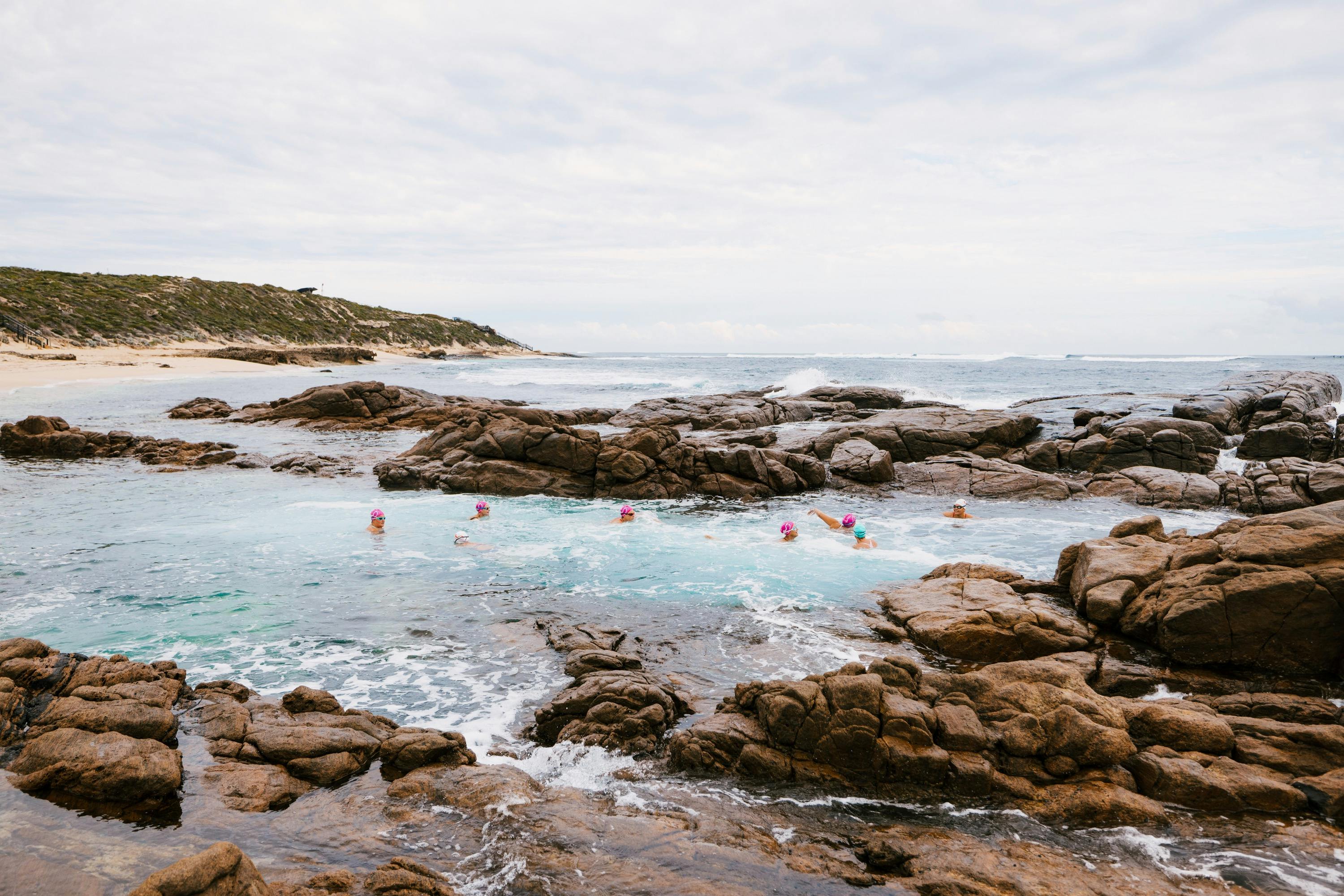coloured swim caps bobbing in a rock pool surrounded by large granite boulders
