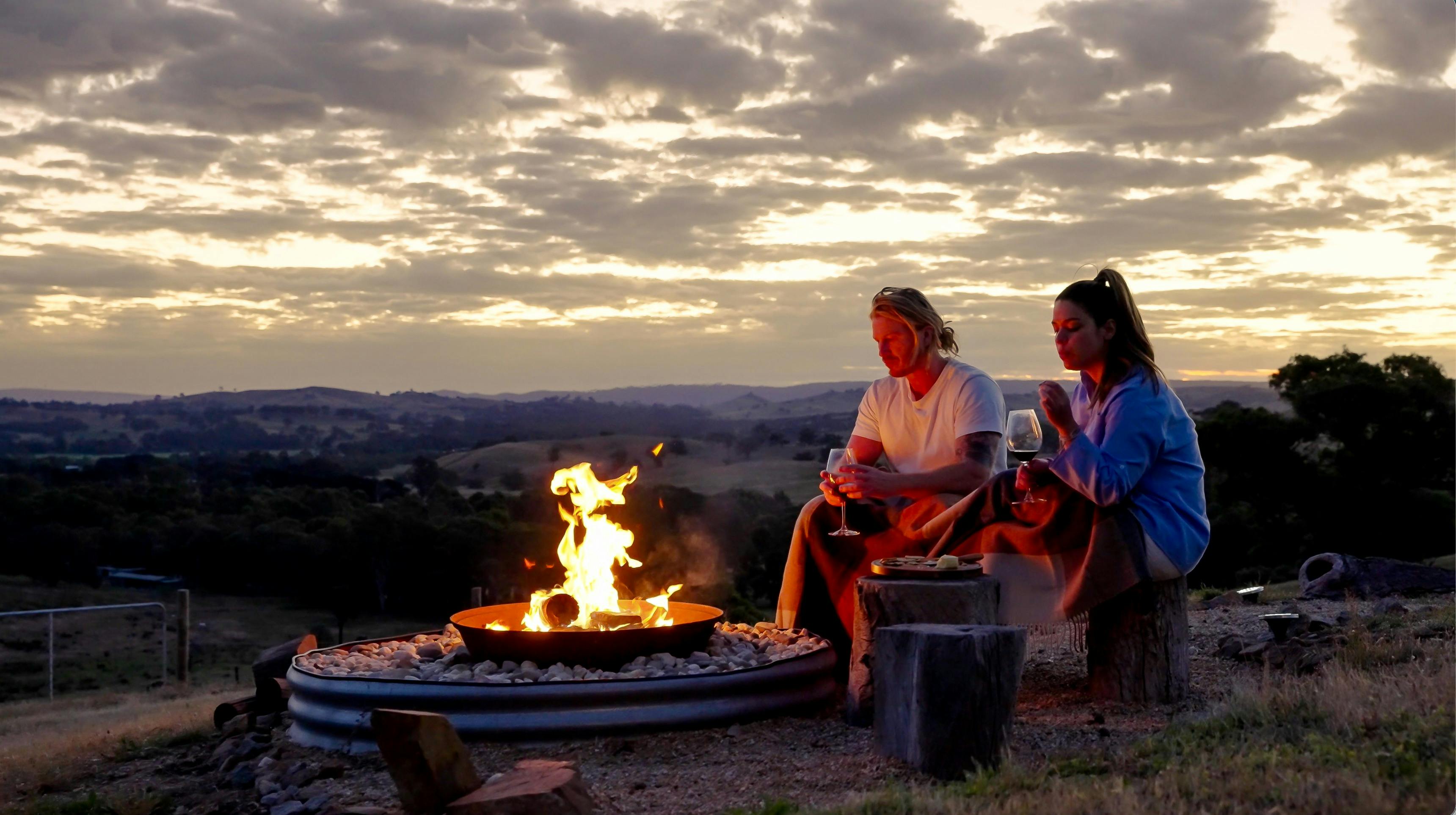 Man and woman warming up by a fire overlooking huge valley in distance