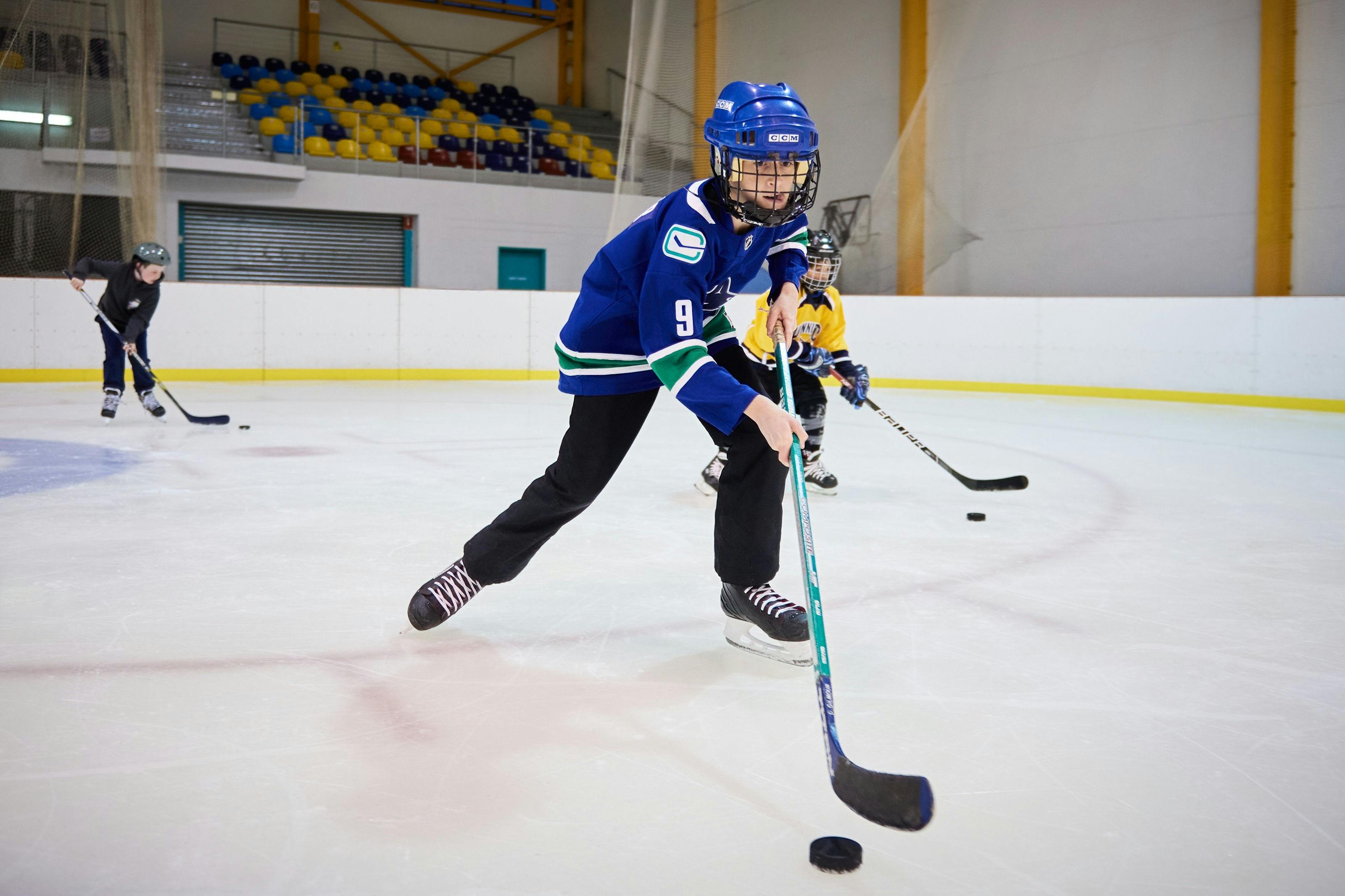 Boy wearing Ice Hockey gear holding stick and skating along with puck