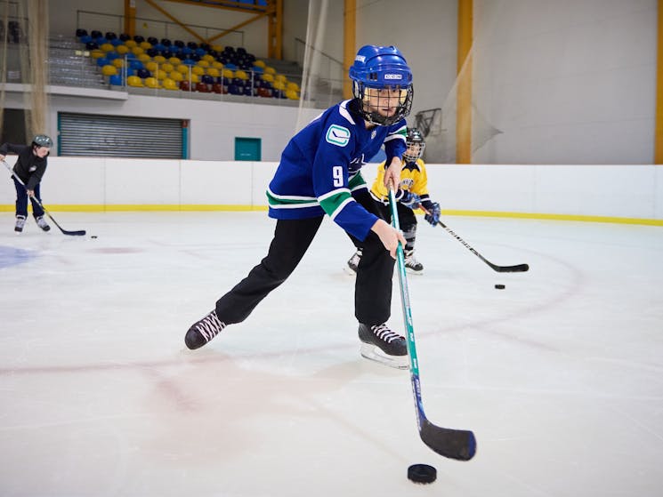 Boy wearing Ice Hockey gear holding stick and skating along with puck