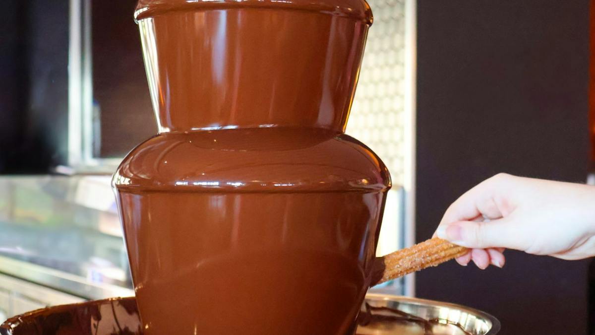 Hand dipping a churro into a chocolate fountain at Chocolate Afternoon  Tea