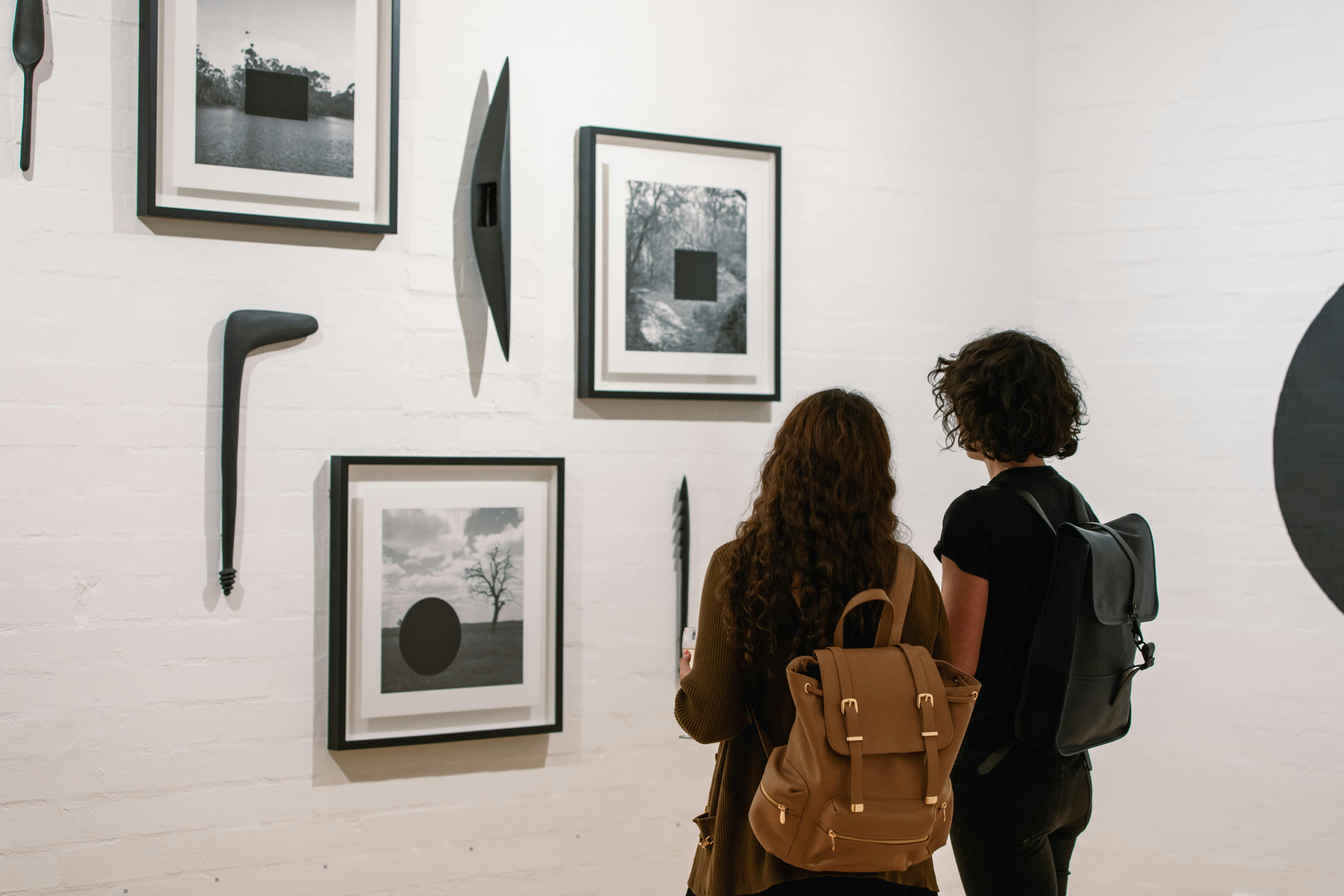 Two women are looking at framed photographs on the gallery wall
