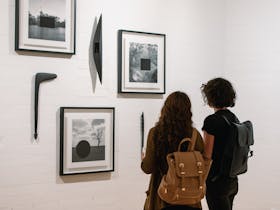 Two women are looking at framed photographs on the gallery wall