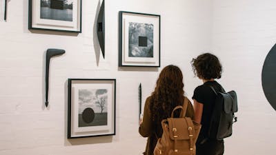 Two women are looking at framed photographs on the gallery wall