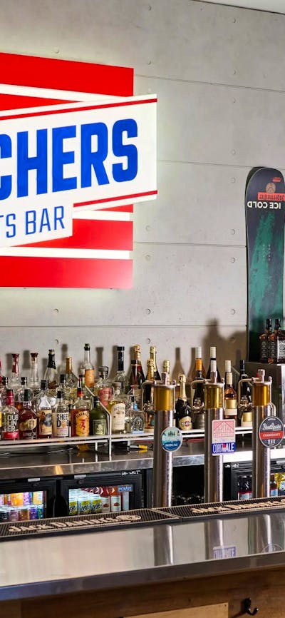 Lines of bottles along a bar with a bright sign in the background