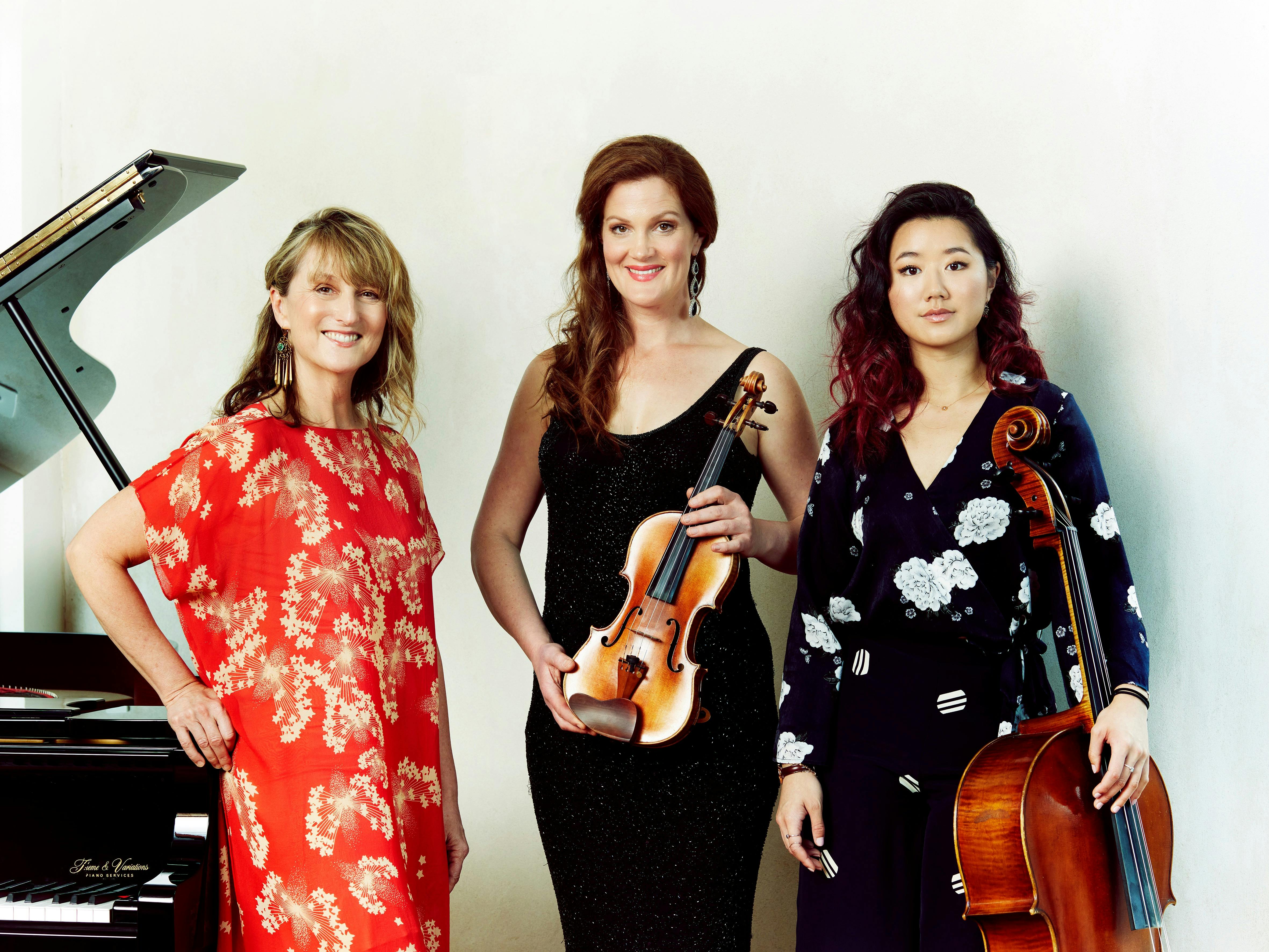 3 women in front of a piano holding instruments