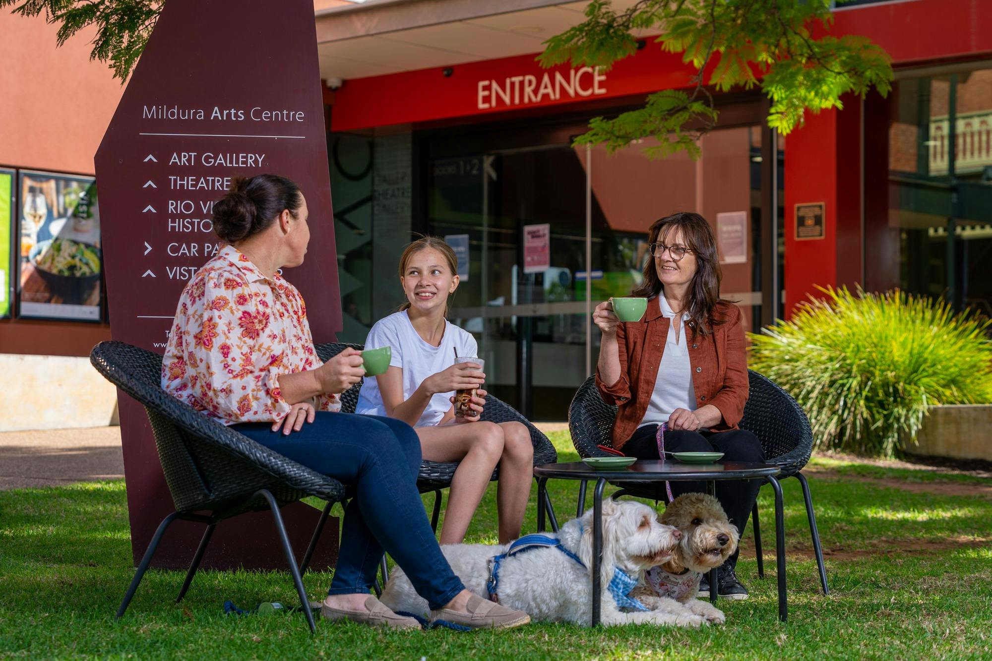 Three people sitting outside with coffees with two dogs