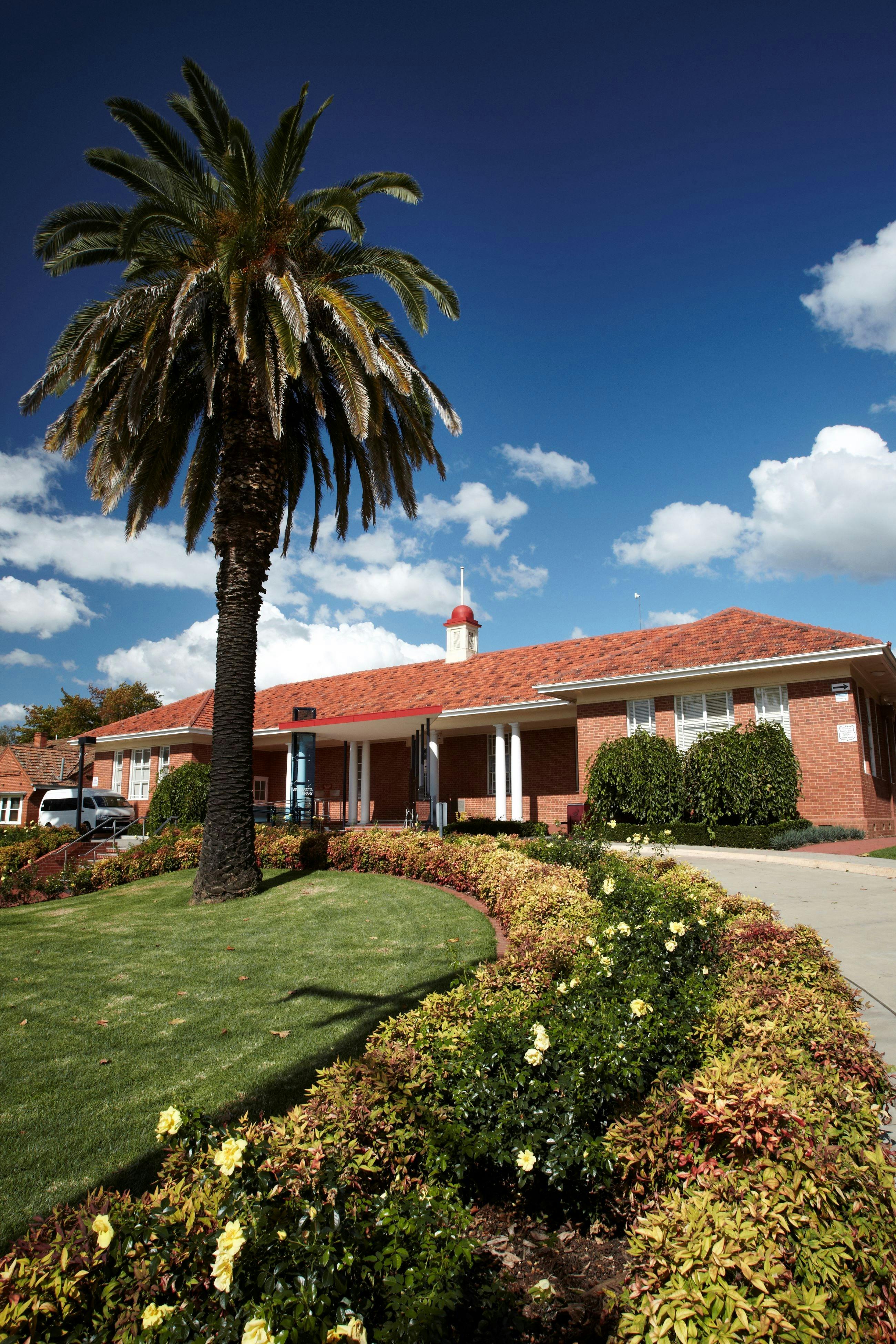 Historic red brick building, driveway, palm tree, lawn and flower garden