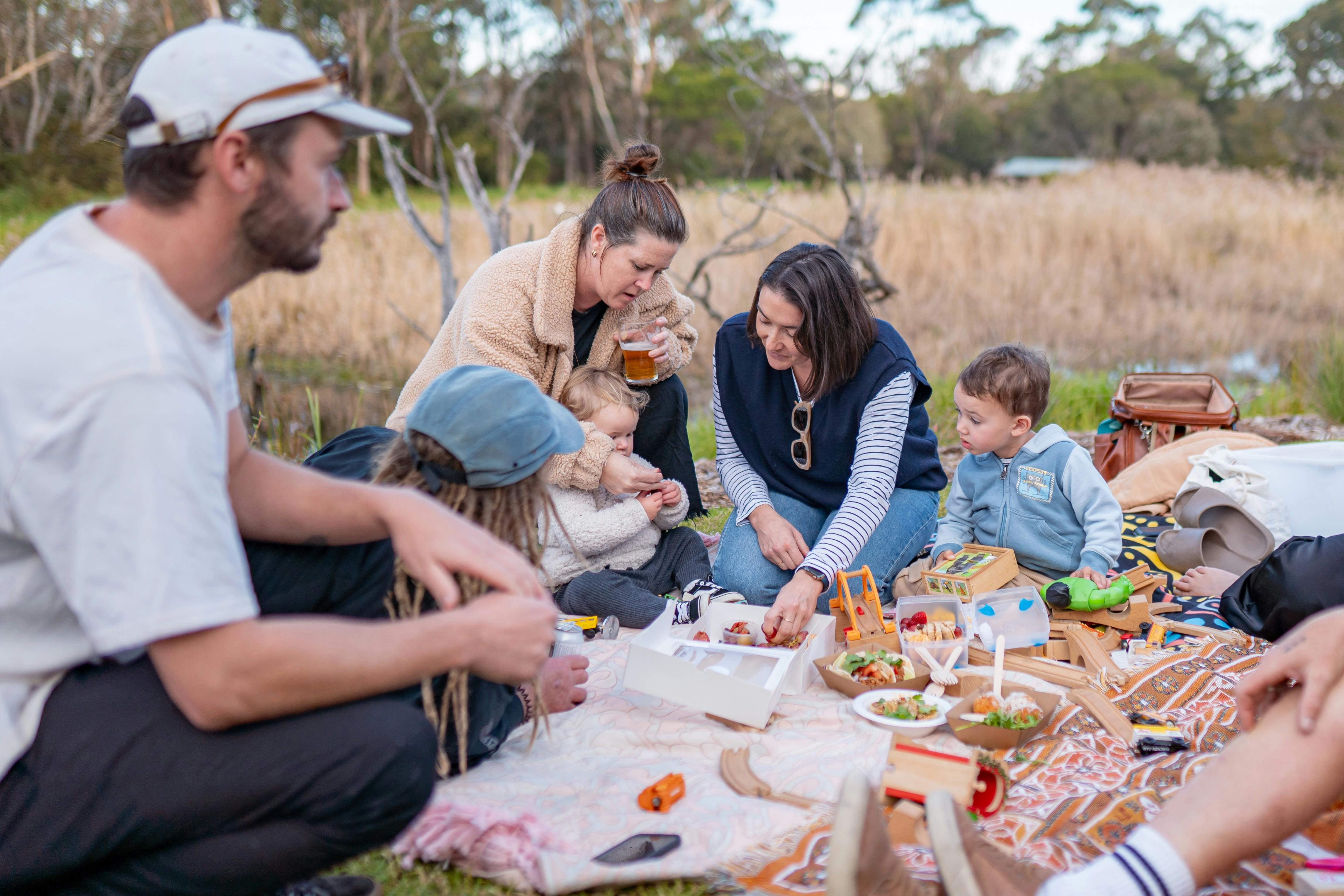 A family sitting on a blanket on the lawn with the Panboola Wetlands behind