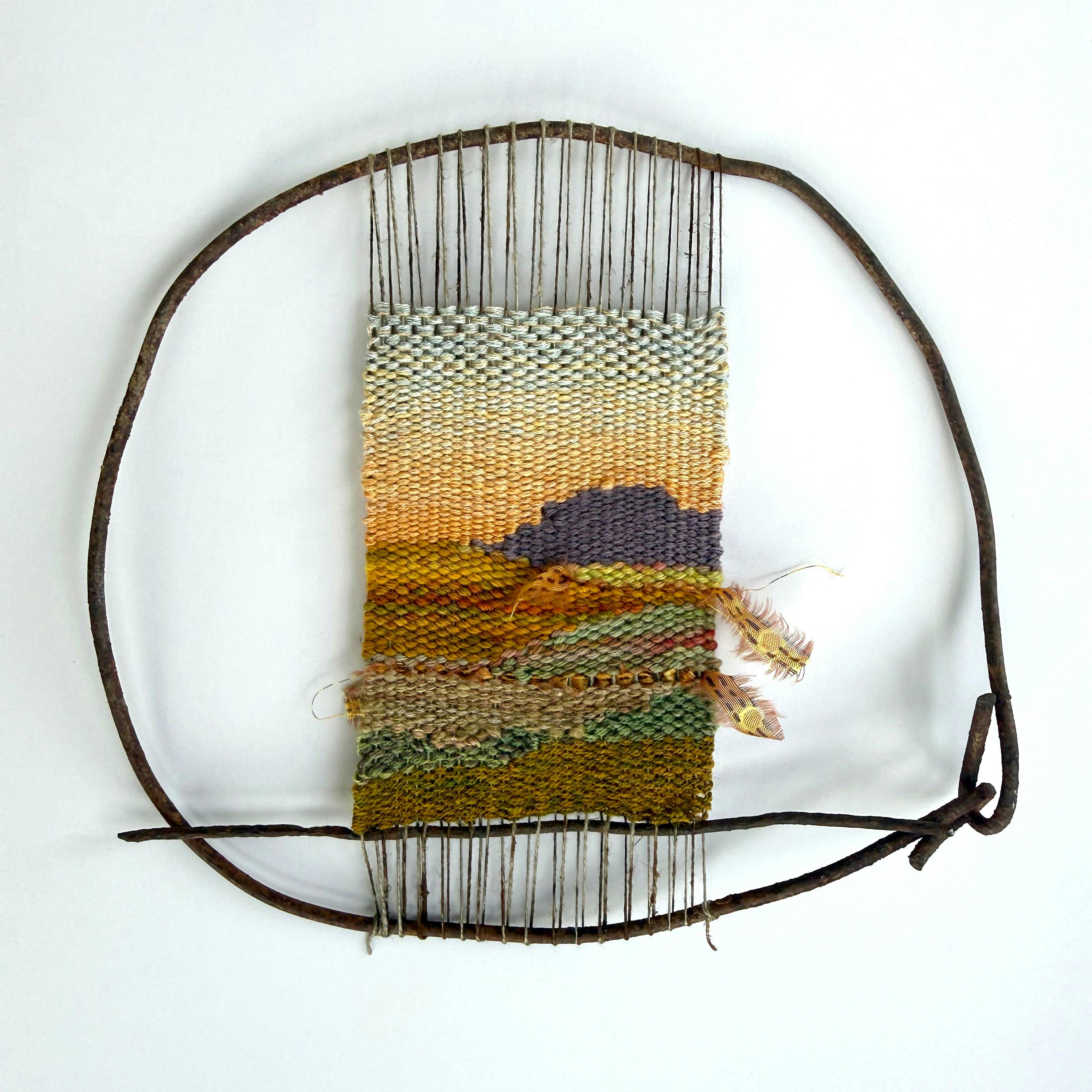 A woven tapestry of a sunset, held within a circular wire frame