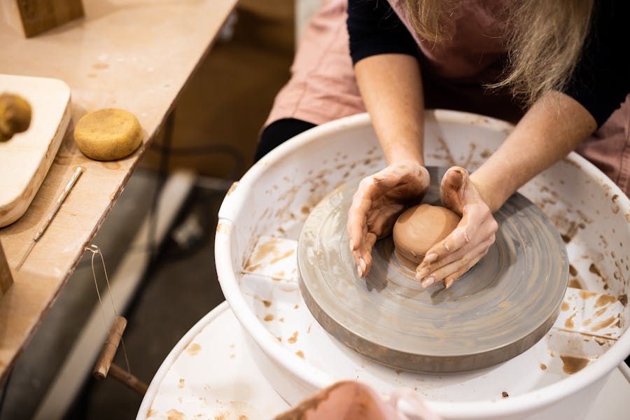 Photo of hands around a ball of clay on the pottery wheel