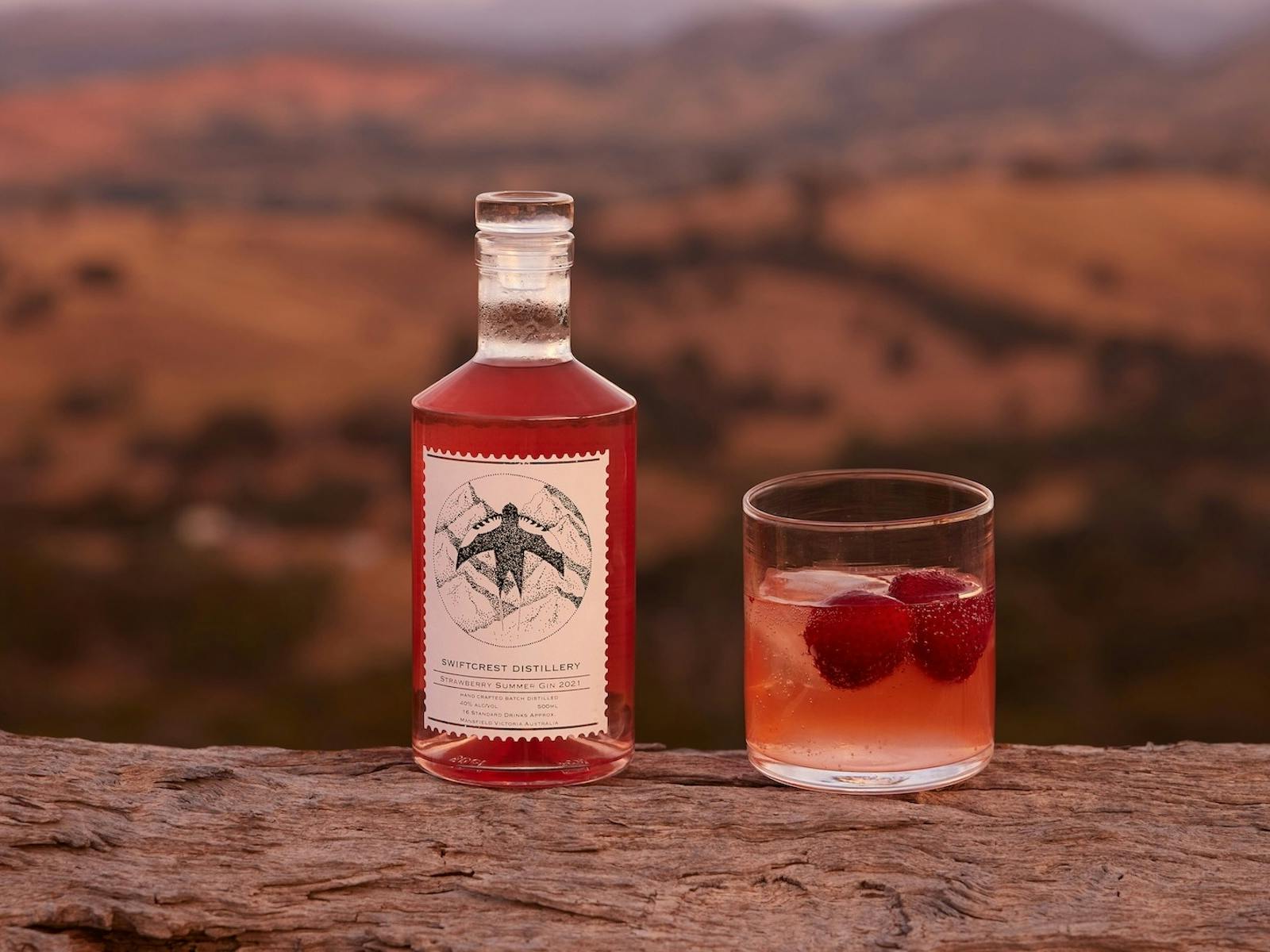 Swiftcrest Distillery strawberry gin bottle and a cocktail glass with fresh strawberries