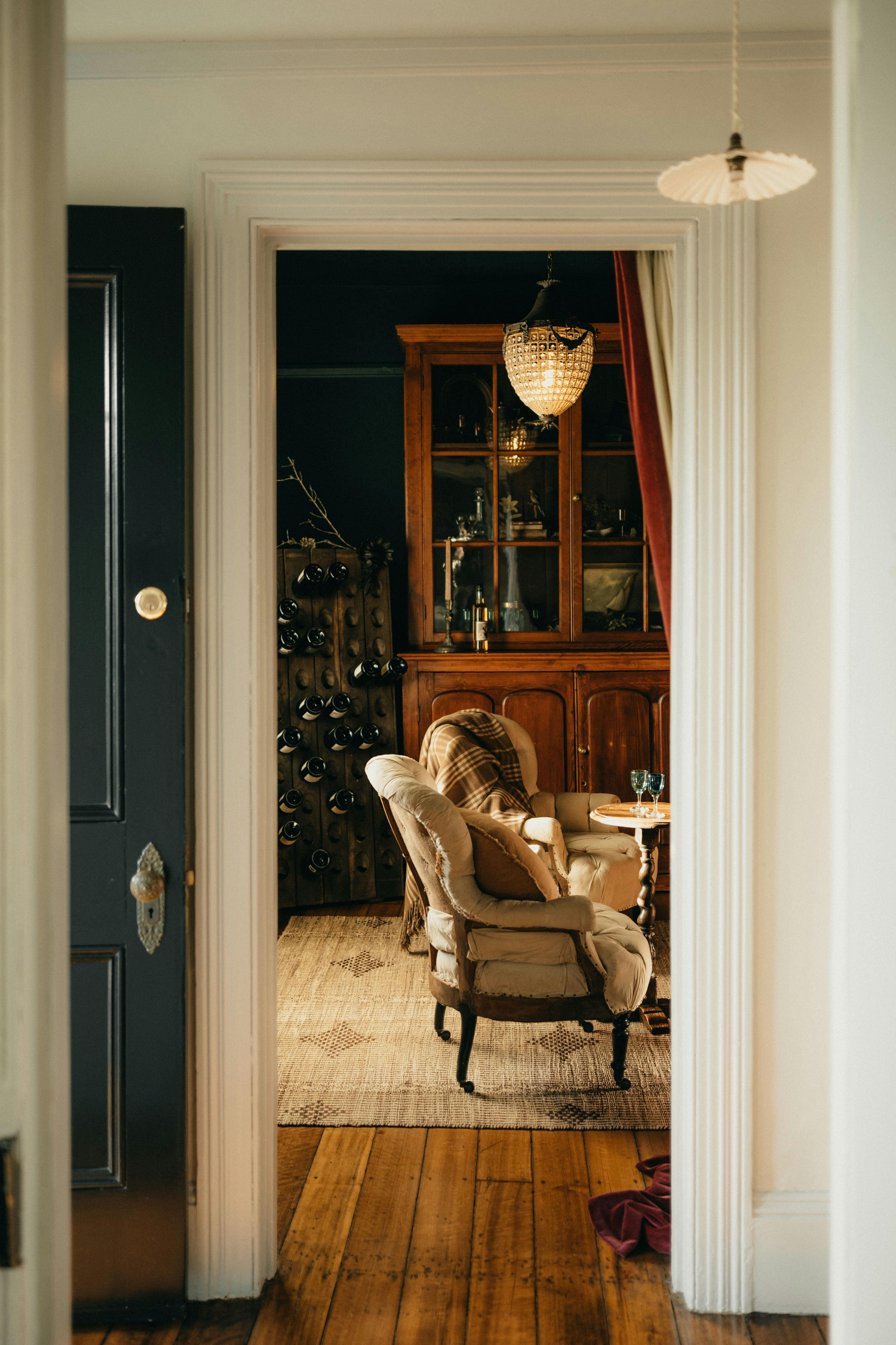View through doorway to sitting room with armchairs, antiques and soft light.