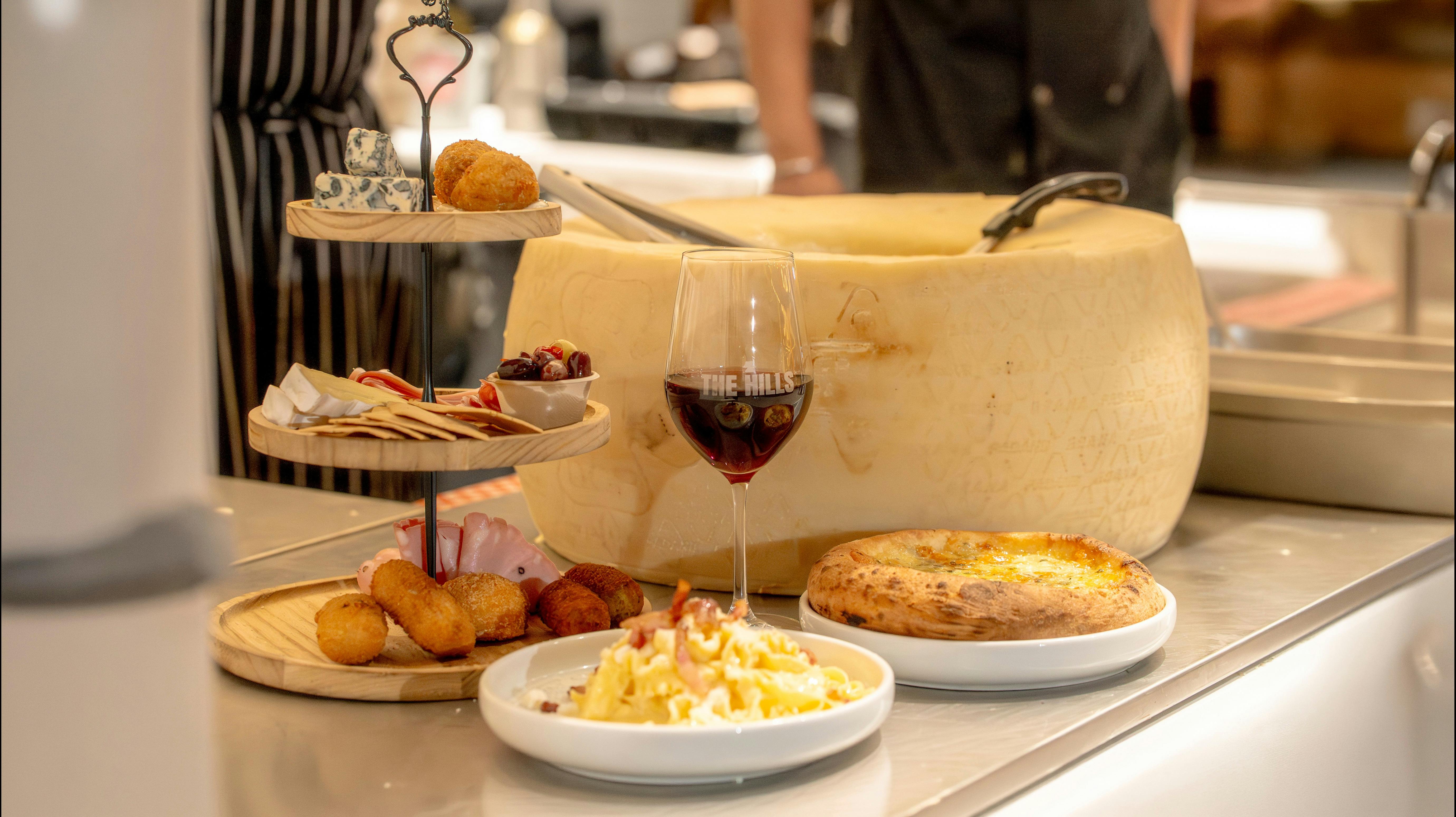 Cheese wheel display with pizza, appetizers, and wine at an Italian restaurant.