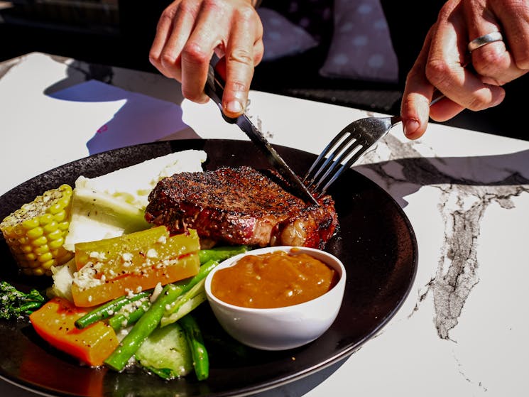 Man cutting into a steak on a black plate with vegetables