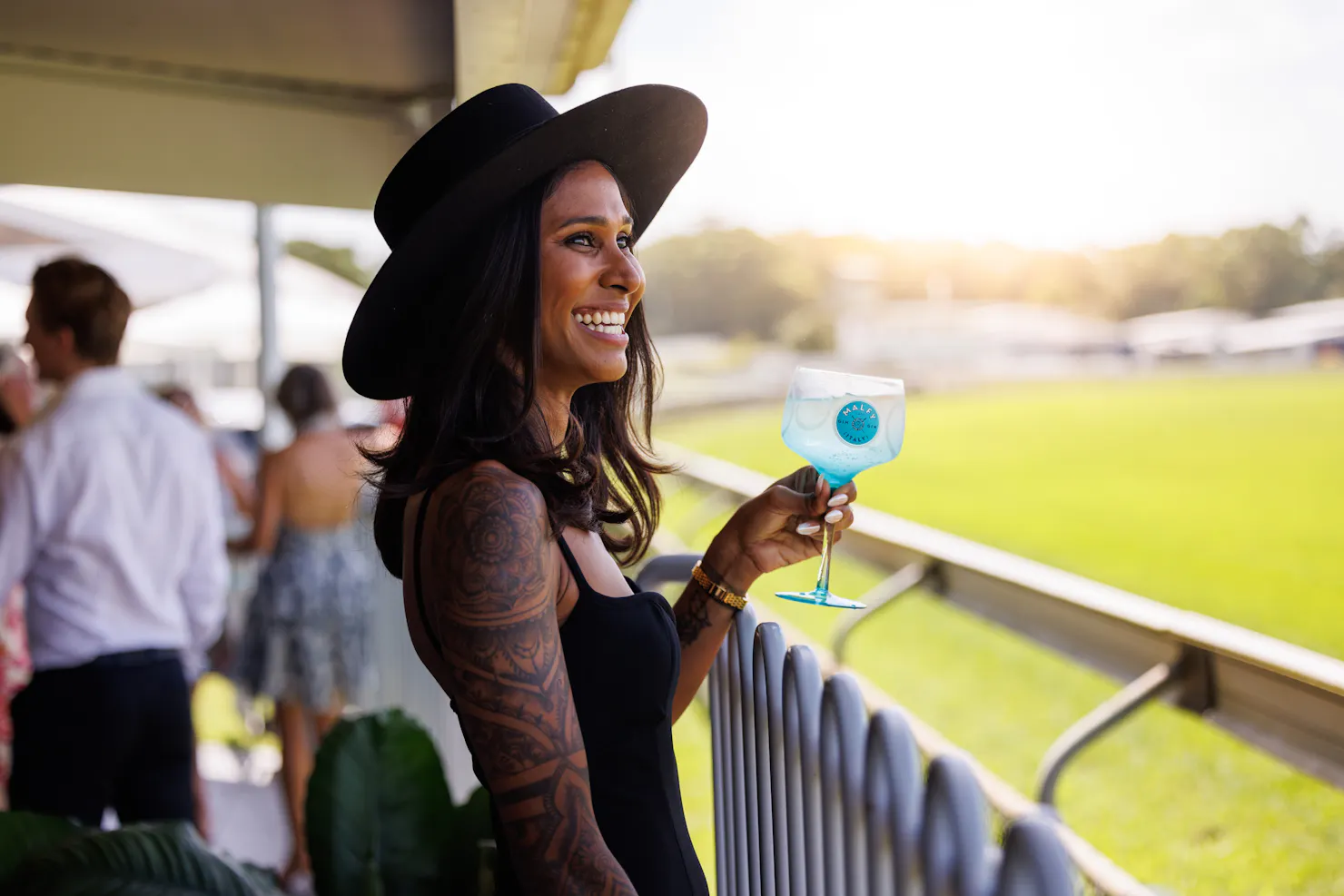 Lady in a hat looking out onto the track holding a cocktail glass