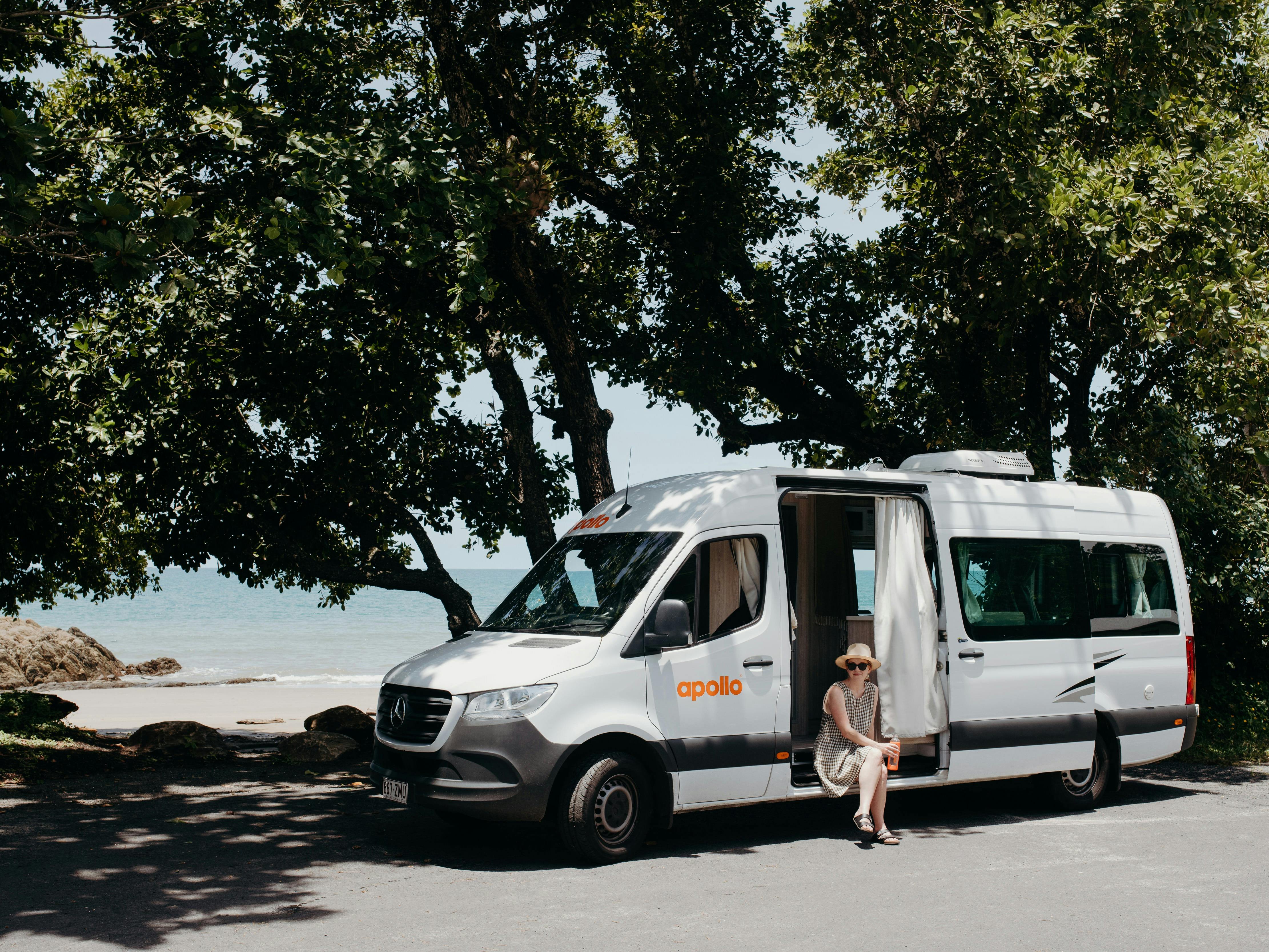 An Apollo Euro Tourer is parked under a tree by the ocean