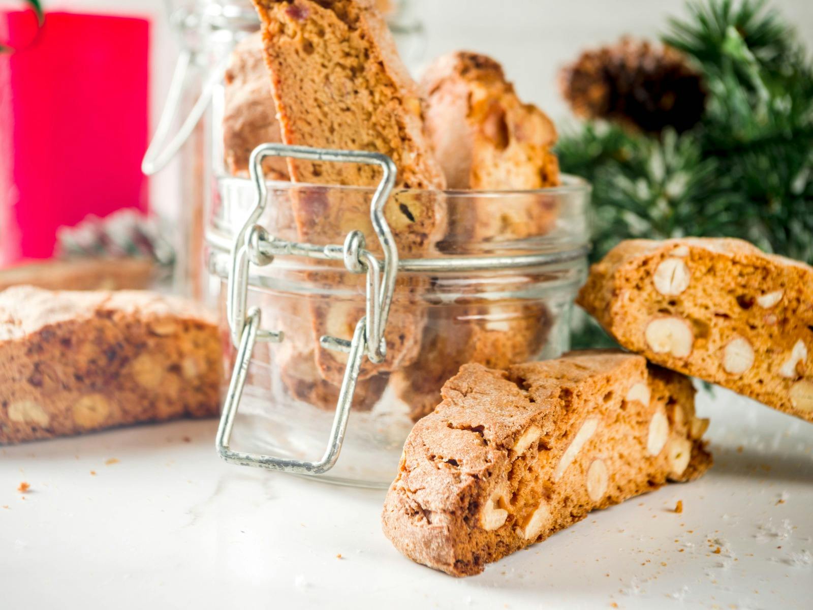 Crispy biscotti pieces standing upright in a clip top jar and other loose pieces on bench.