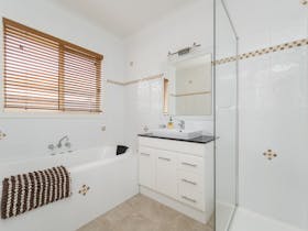 Image of bathroom with glass framed shower, separate bath, single vanity unit, tiled floor and walls