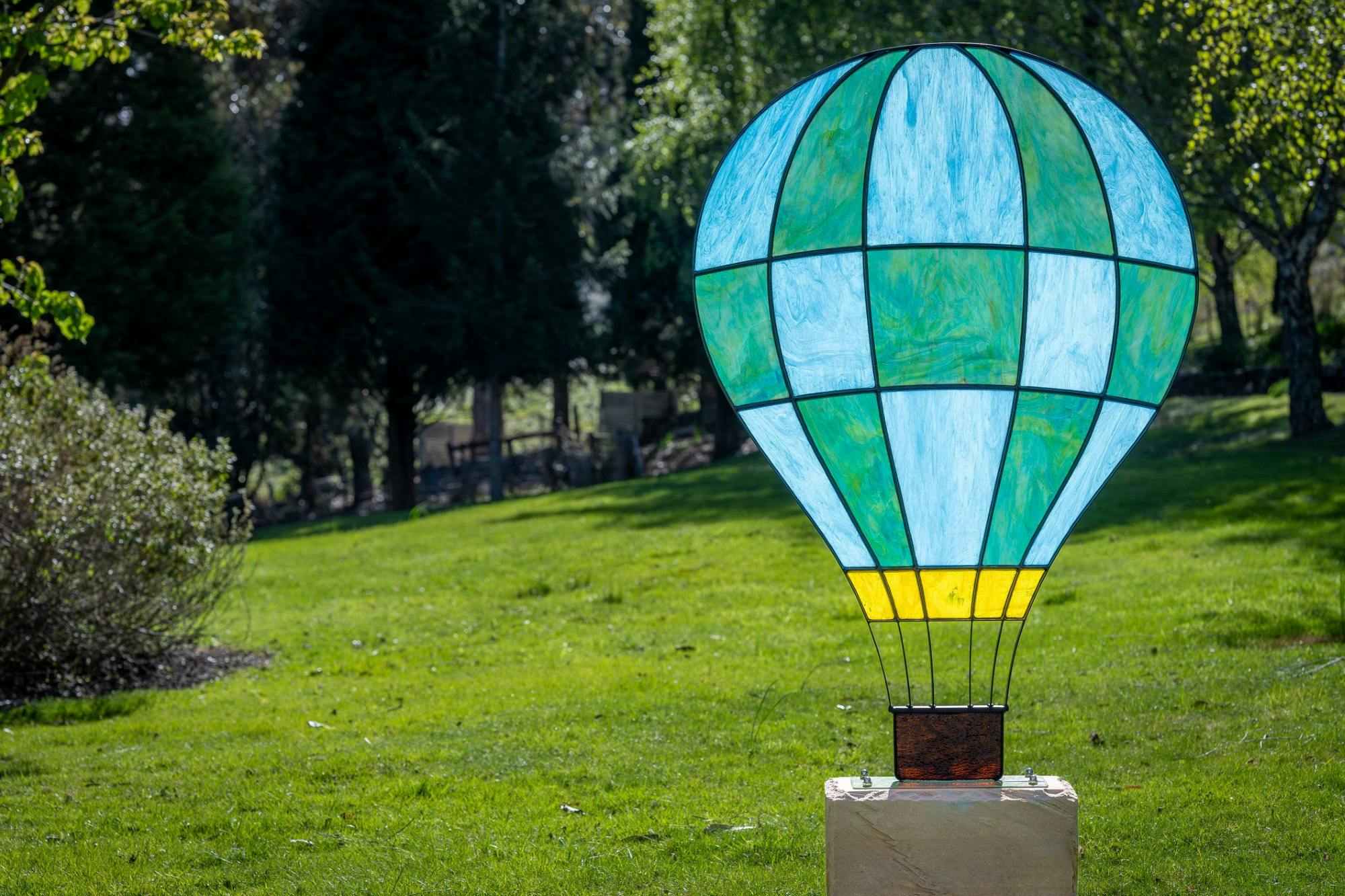 Stained glass hot air balloon sculpture displayed in a garden.