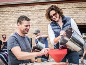 Small Batch Wine Making by Steven & Emma Raidis. Pouring wine into barrel after pressing.
