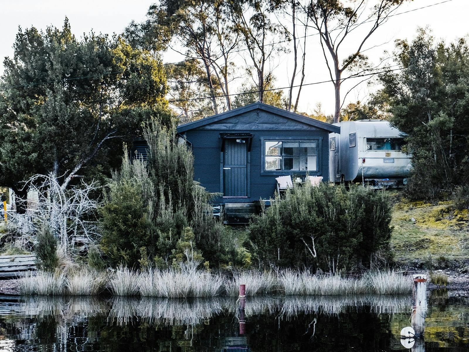 A black shack nestled in nature surrounded by trees, on the shore of Lettes Bay.