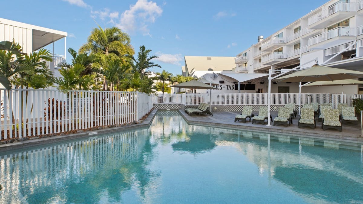 Pool area at Airlie Beach Hotel featuring sun loungers, tropical landscaping, a crystal-clear water