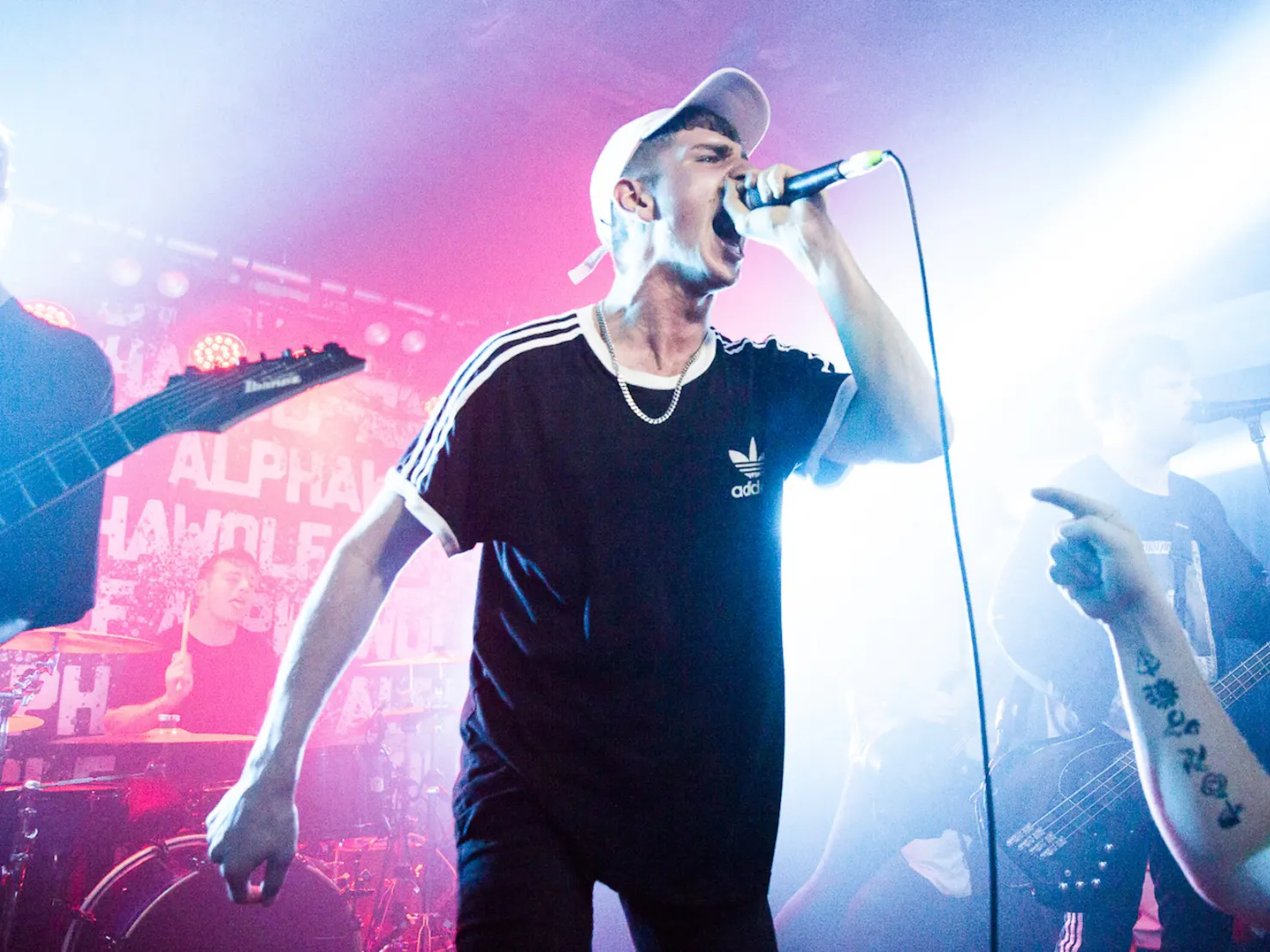 Lead singer standing and singing into a microphone with blue and pink lights