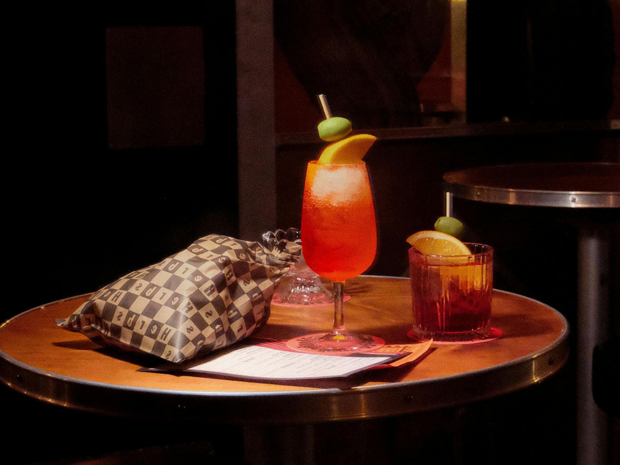 Table with a spritz and Negroni garnished with olives and orange, served with popcorn and menu.