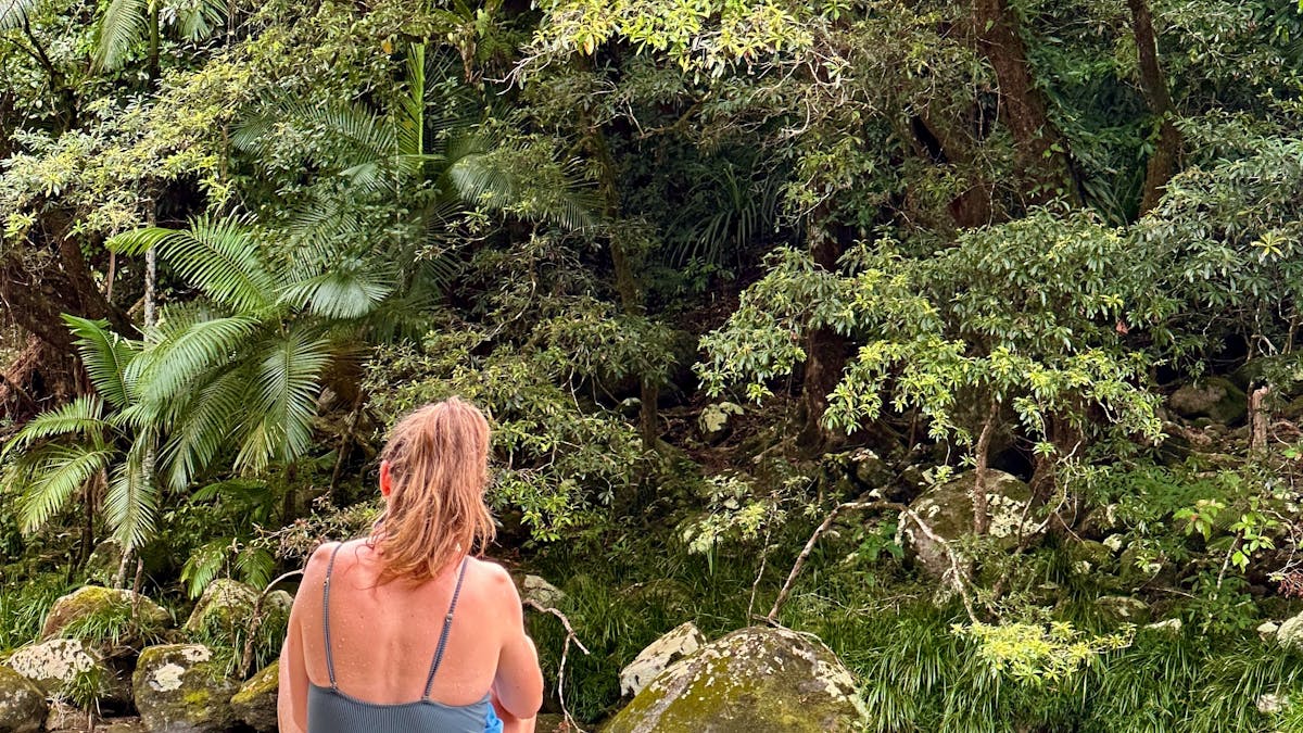 Woman sits on Granite Boulder in Mossman Gorge swimming area in Tropical North Queensland Woman sits on Granite Boulder in Mossman Gorge swimming area in Tropical North Queensland