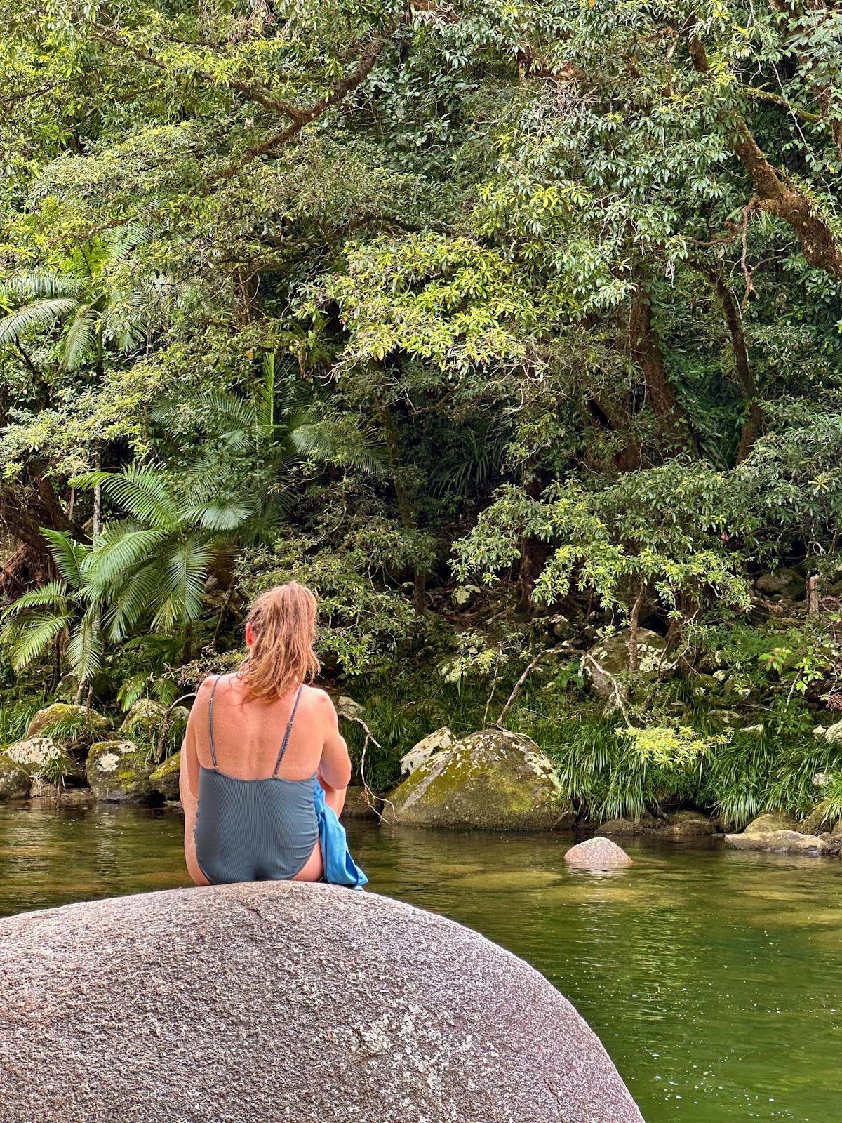 Woman sits on Granite Boulder in Mossman Gorge swimming area in Tropical North Queensland