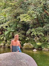 Woman sits on Granite Boulder in Mossman Gorge swimming area in Tropical North Queensland