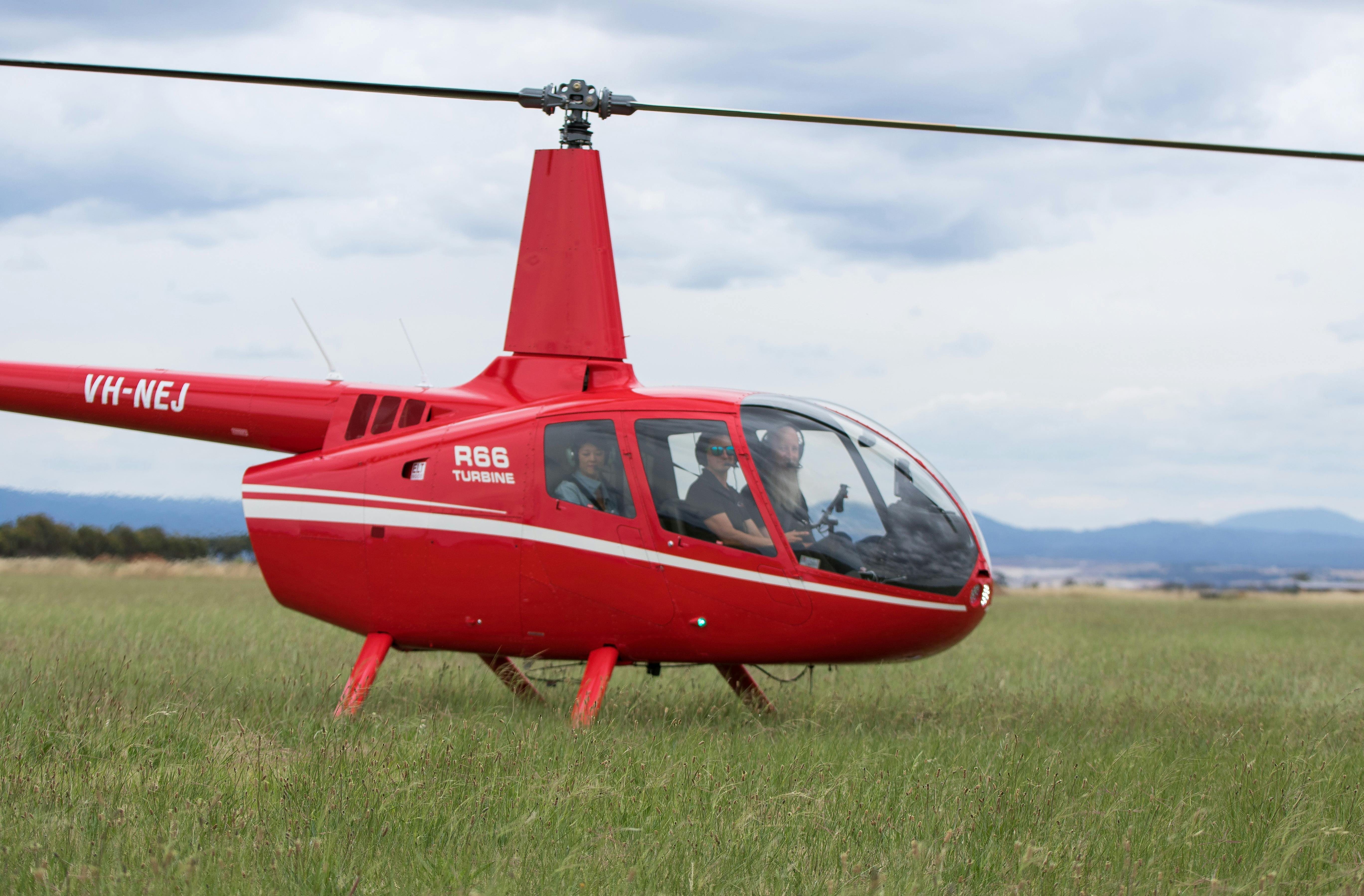 Red Robinson R66 Helicopter parked in a grassy field.