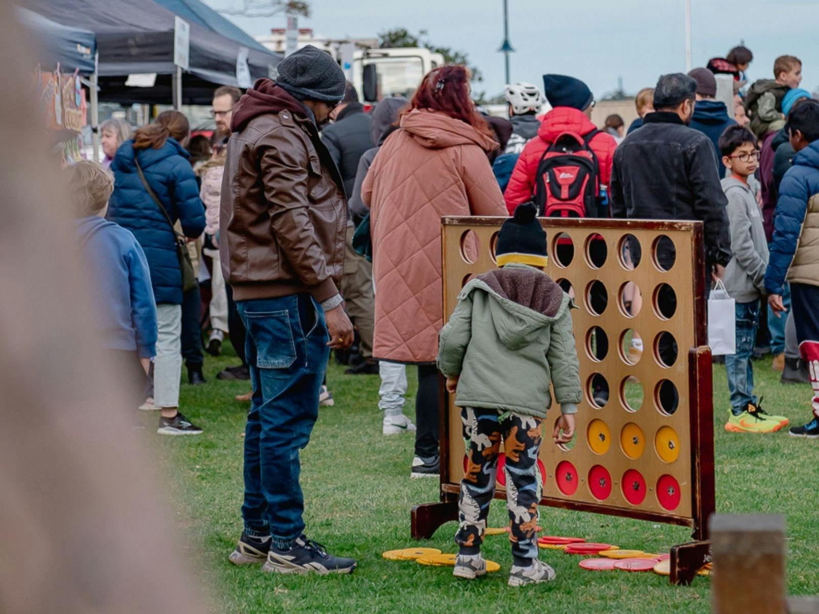 A parent and child playing giant connect 4 lawn game with crowd behind