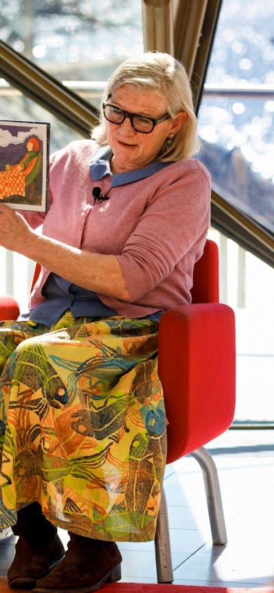 Woman sitting on a chair holding a book reading to a group of children.