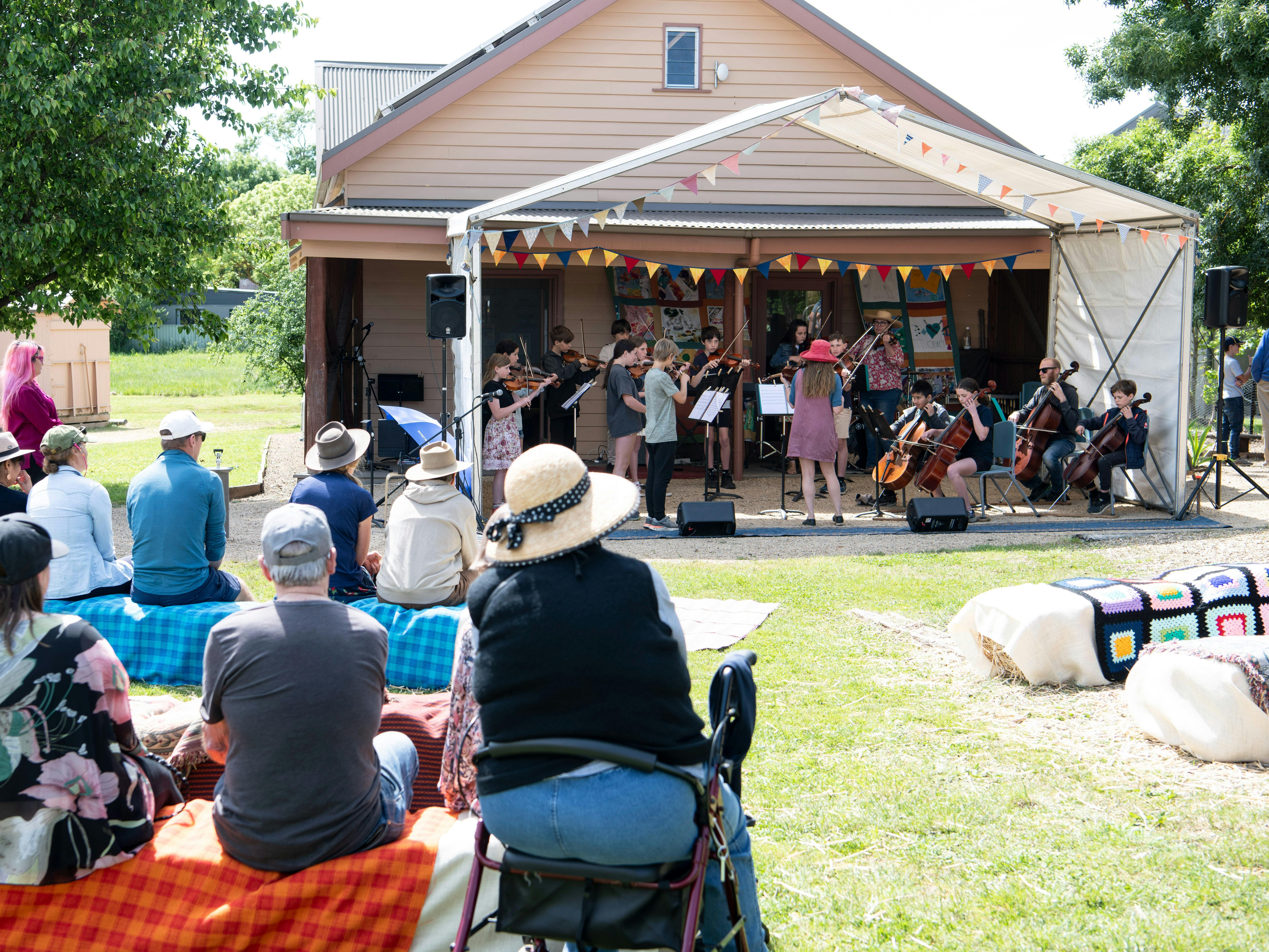 people sitting on straw bales enjoying one of the school string orchestras