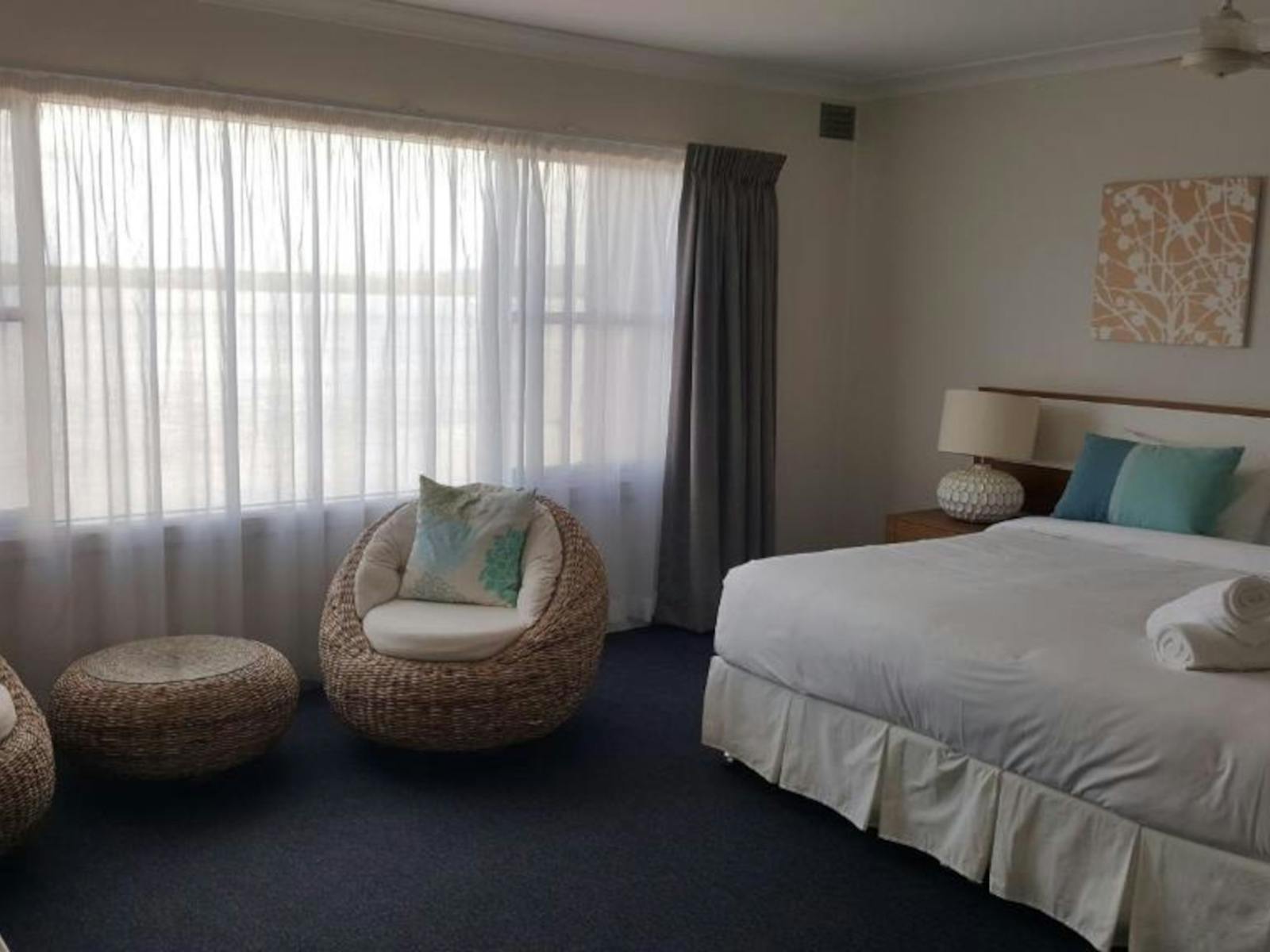 Large bedroom with cane comfy chairs and big bed with cushions