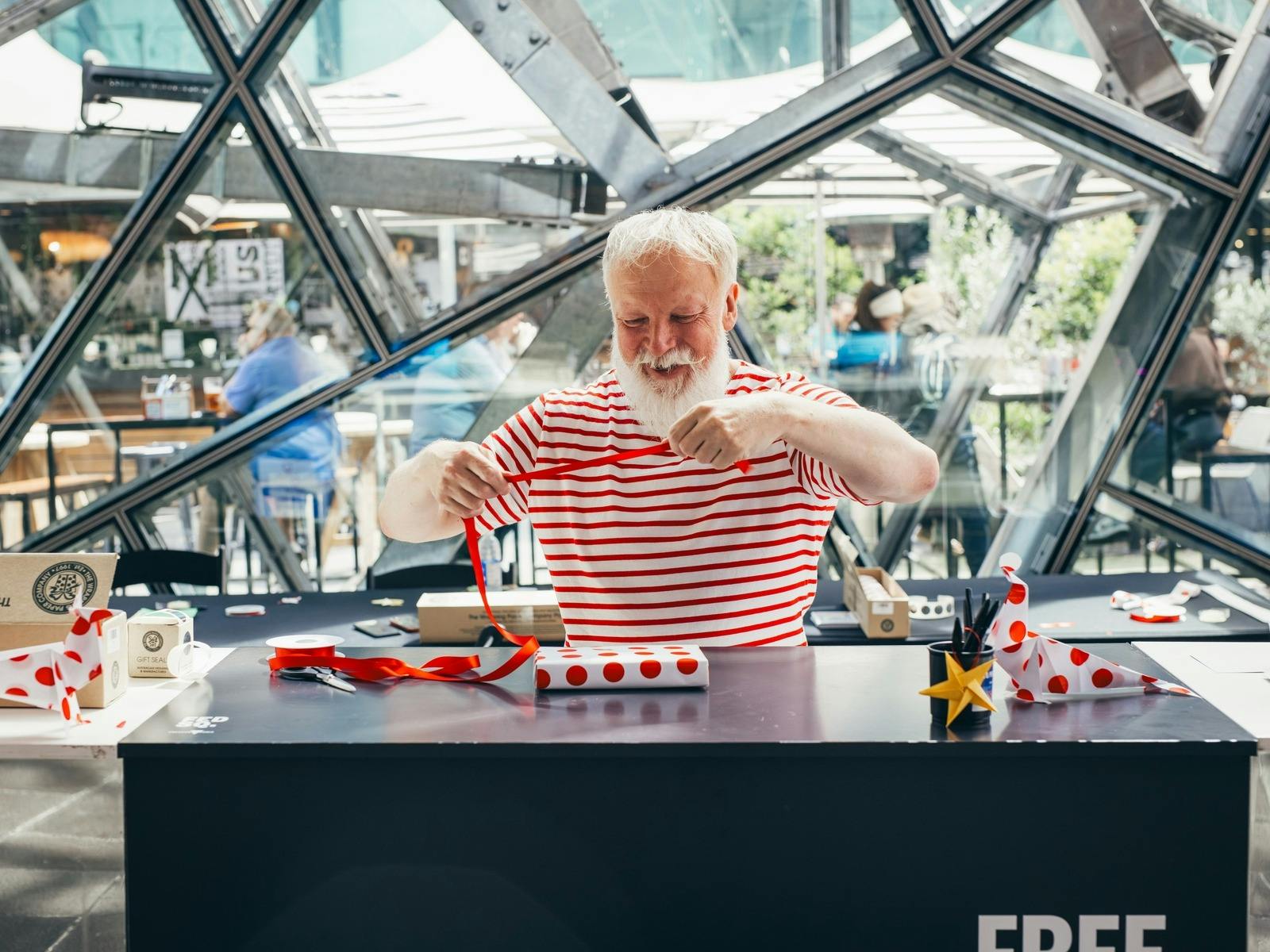 A man dressed in red and white is wrapping a christmas present on a table