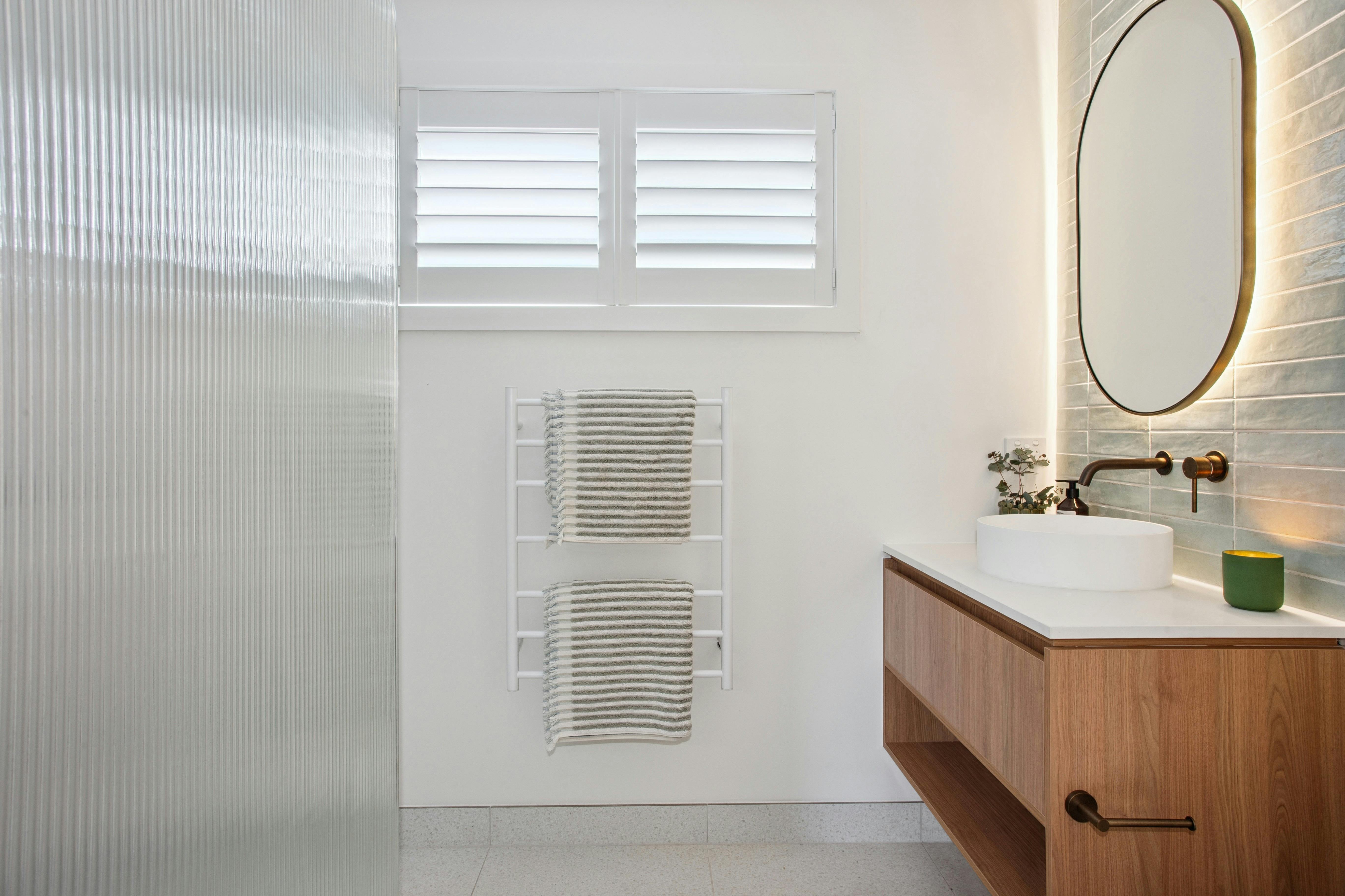 Timber vanity, round white basin, brushed bronze tapware, oval back mirrorlit mirror and soft green
